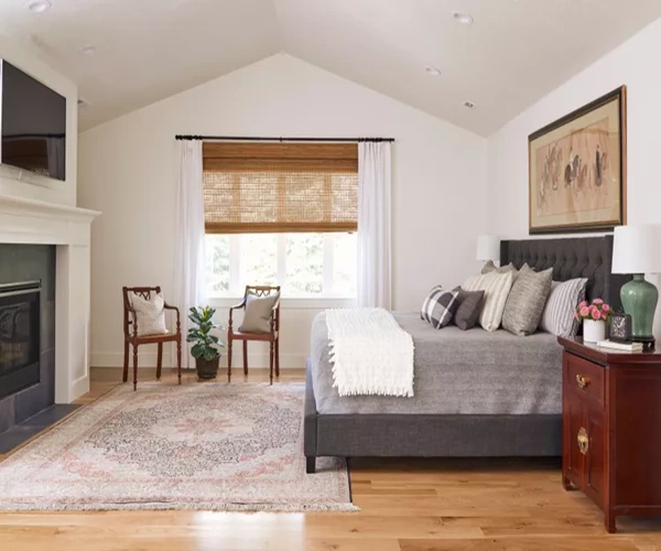 Spacious bedroom features a patterned rug, fireplace, and vaulted ceiling.